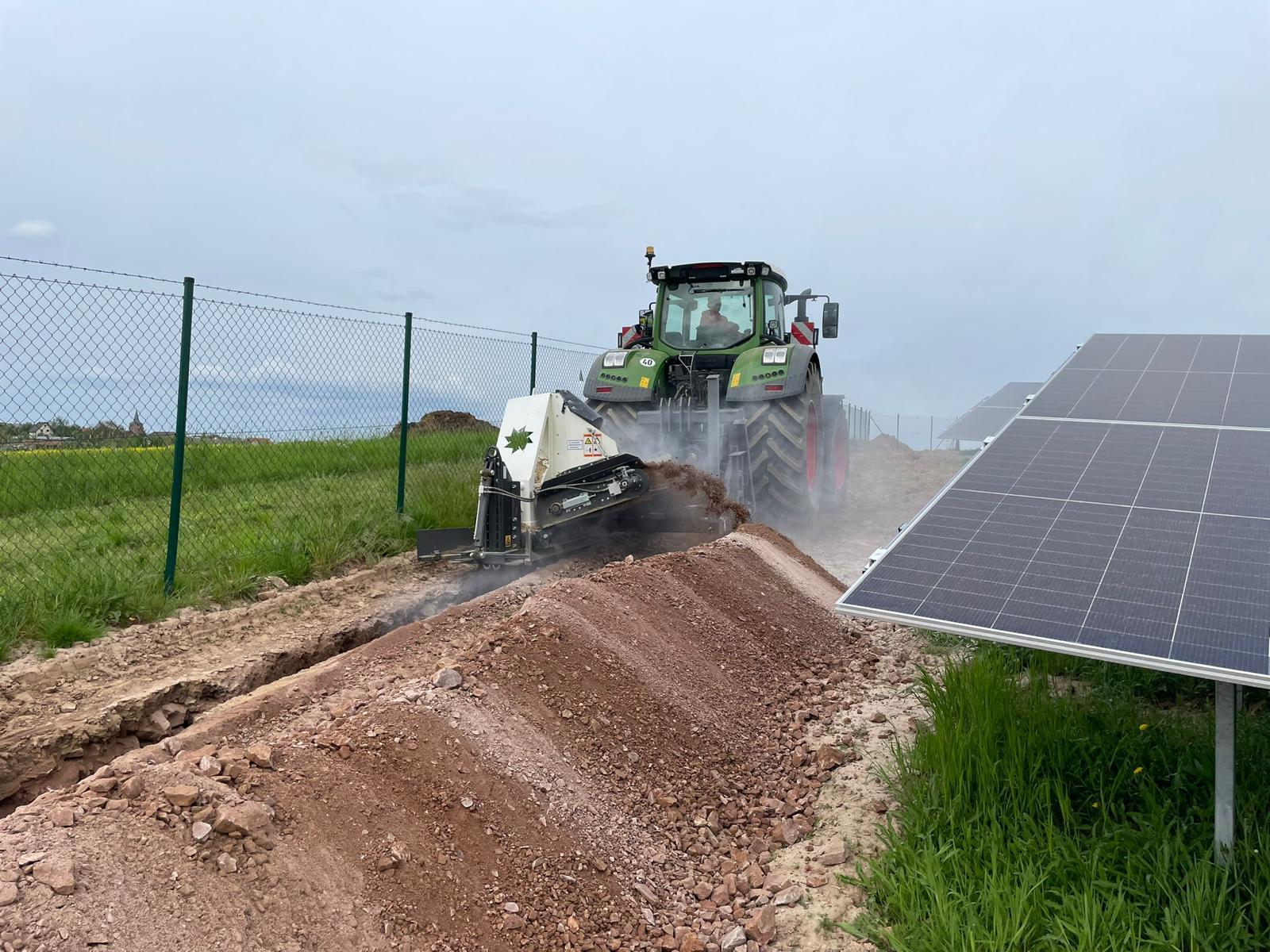 Traktor mit Grabenfräse neben Solarpanelen auf der Baustelle