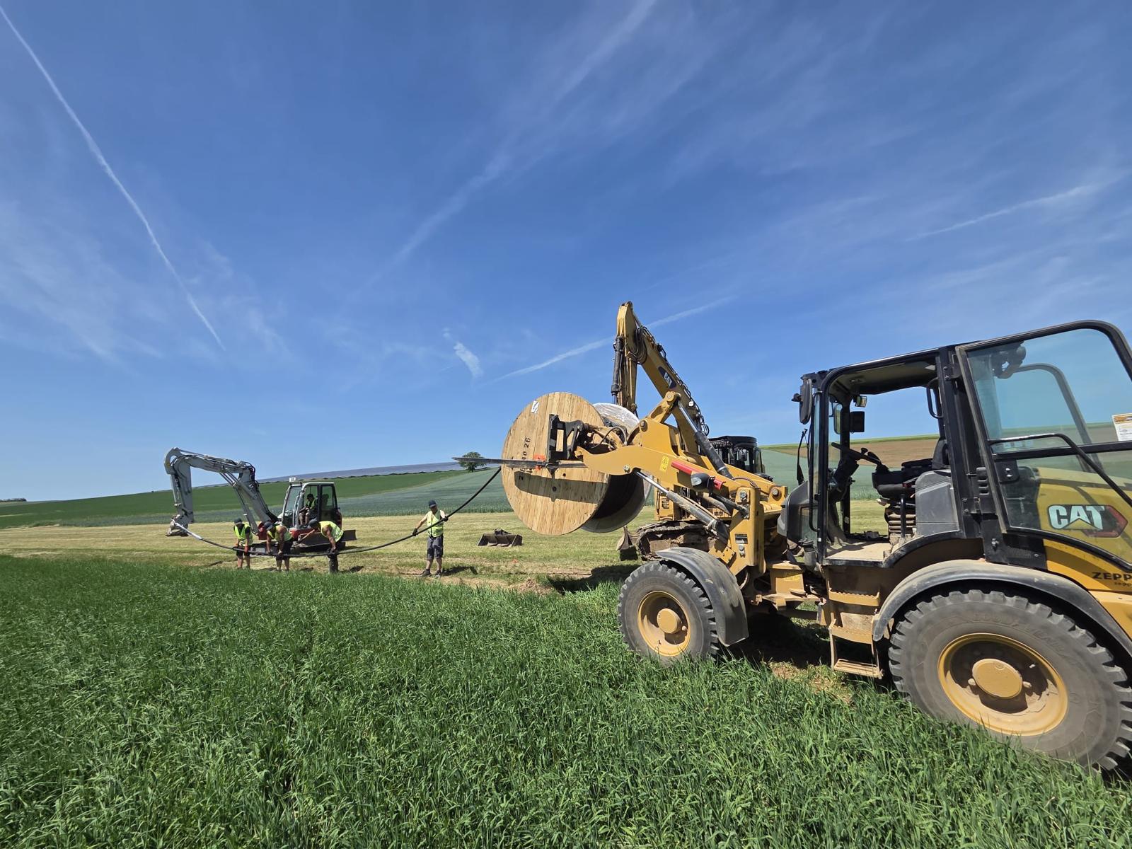 CAT Radlader mit großer Kabeltrommel und Arbeitern auf dem Feld